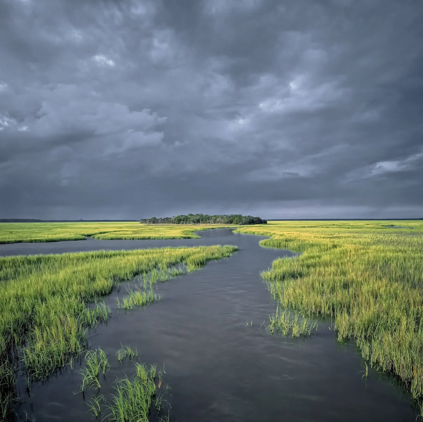 A tidal creek winding through coastal salt marsh under storm clouds
